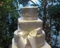 A mix of square and round tiers of cake stacked in the classic wedding cake form. All tiers are covered in white fondant with intricate buttercream detail. White ribbons add elegance and sophistication. 