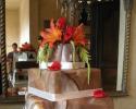 Three square tiers of cake stacked with a beautiful brown and white marble design. Each layer has a white strip of fondant to separate the layers. Flowers in red and orange colors sit on top of the cake for decoration.