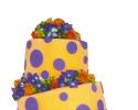 Three tiered crooked polka-dot cake. Orange and purple fondant decorate the cake with blue and orange flowers. Fun, beautiful and unique design! 