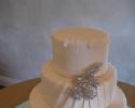 Three tiered cake covered in white fondant with buttercream details on the first and third layers. The second layer sits a silver decorative piece, adding the cake a touch of class and elegance.