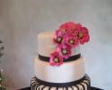 Three tiered cake covered in white fondant. A stripe of black fondant surrounds layers one and two while the third layer of cake shows an amazing zebra-like pattern. Flowers made out of pink fondant add color to this beautiful black and white cake.